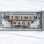 Minimum wage word written on wood block with American Dollar-bills. Directly above.