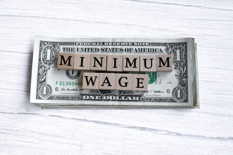 Minimum wage word written on wood block with American Dollar-bills. Directly above.