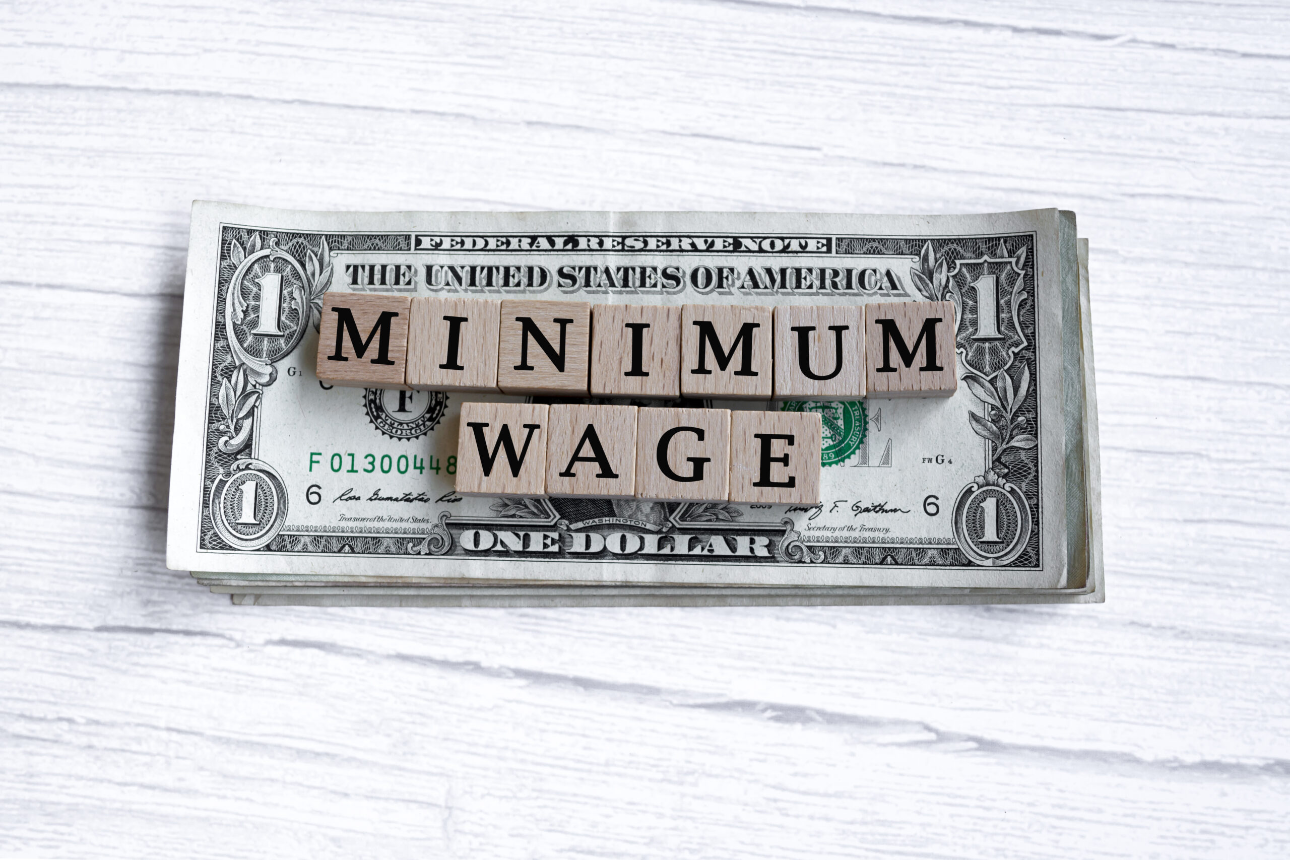 Minimum wage word written on wood block with American Dollar-bills. Directly above.